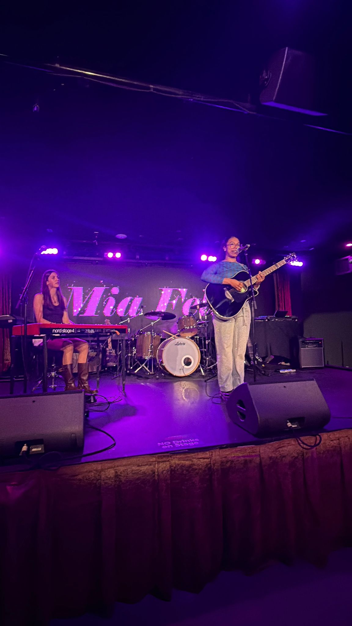 Mia Feliz on stage with her band, purple lights, her name glowing behind her