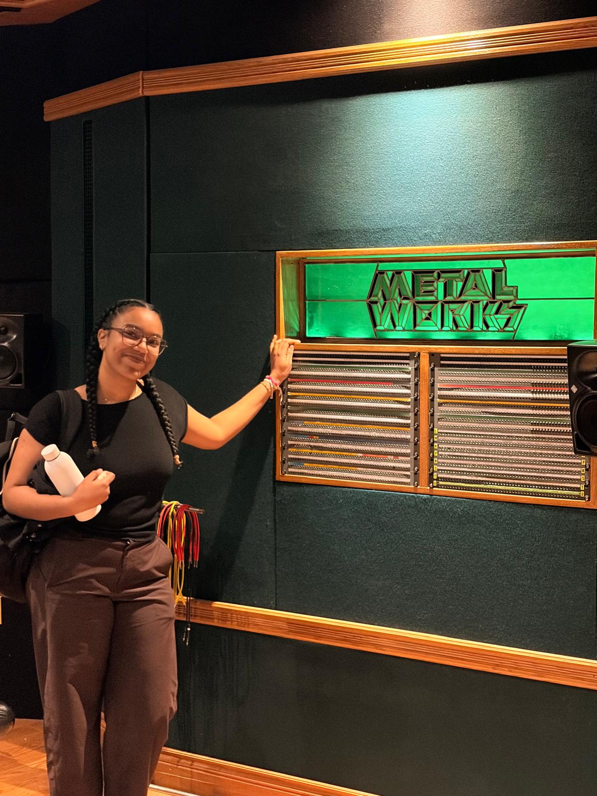 Mia at Metalworks studio, hand on the patchbay under the green sign